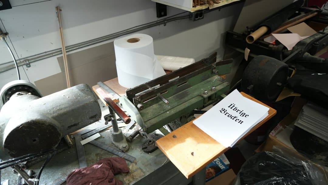 A cluttered workshop table with tools, paper, and machine parts